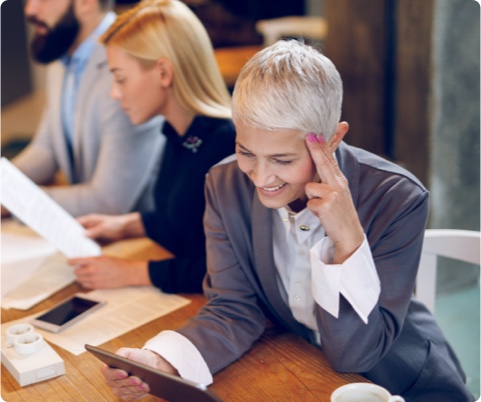 Photo of a woman sitting down and looking at her tablet with colleagues around her